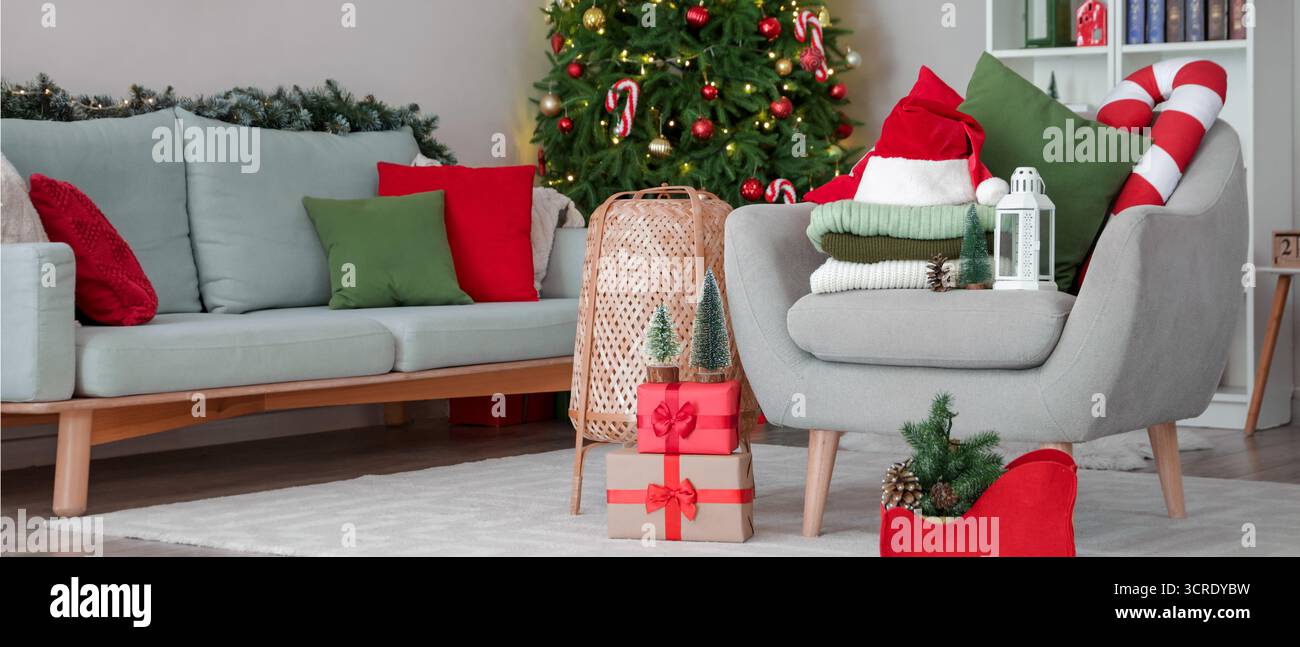 Stack of winter clothes with Christmas decorations and gifts on armchair at home Stock Photo