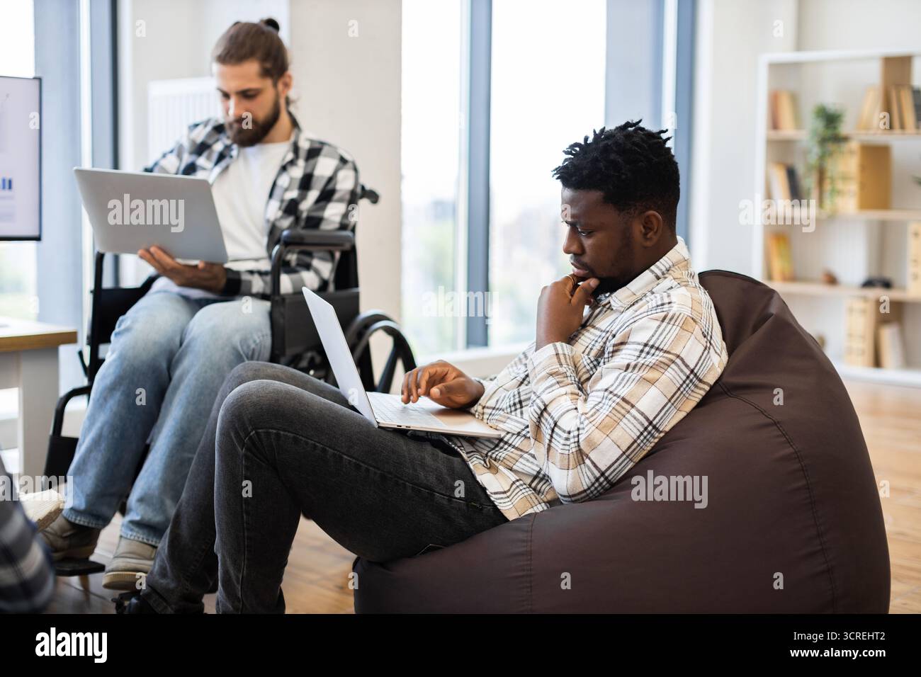 Two professionals collaborating in casual workspace with laptops Stock Photo