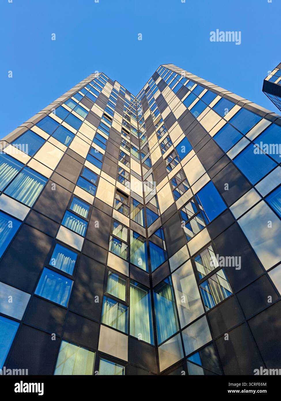 Modern skyscraper facade viewed from the ground, featuring a repeating geometric checkerboard pattern of dark panels and reflective blue glass windows Stock Photo