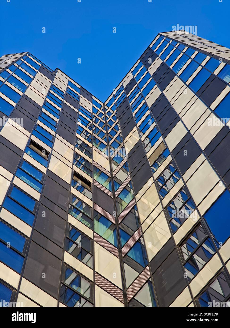 Modern skyscraper facade viewed from the ground, featuring a repeating geometric checkerboard pattern of dark panels and reflective blue glass windows Stock Photo