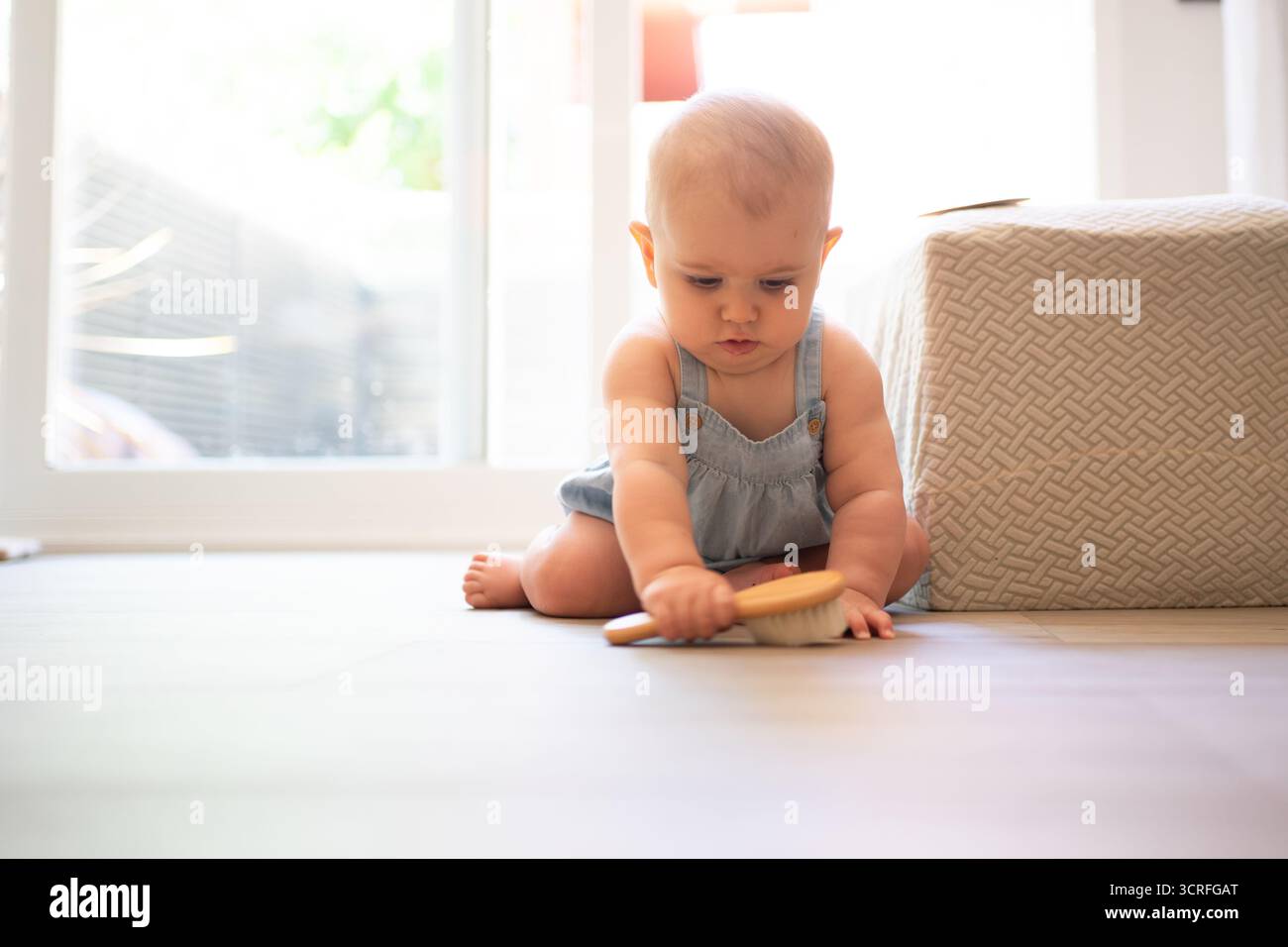 Cute baby girl sitting on the floor playing with a hairbrush Stock Photo