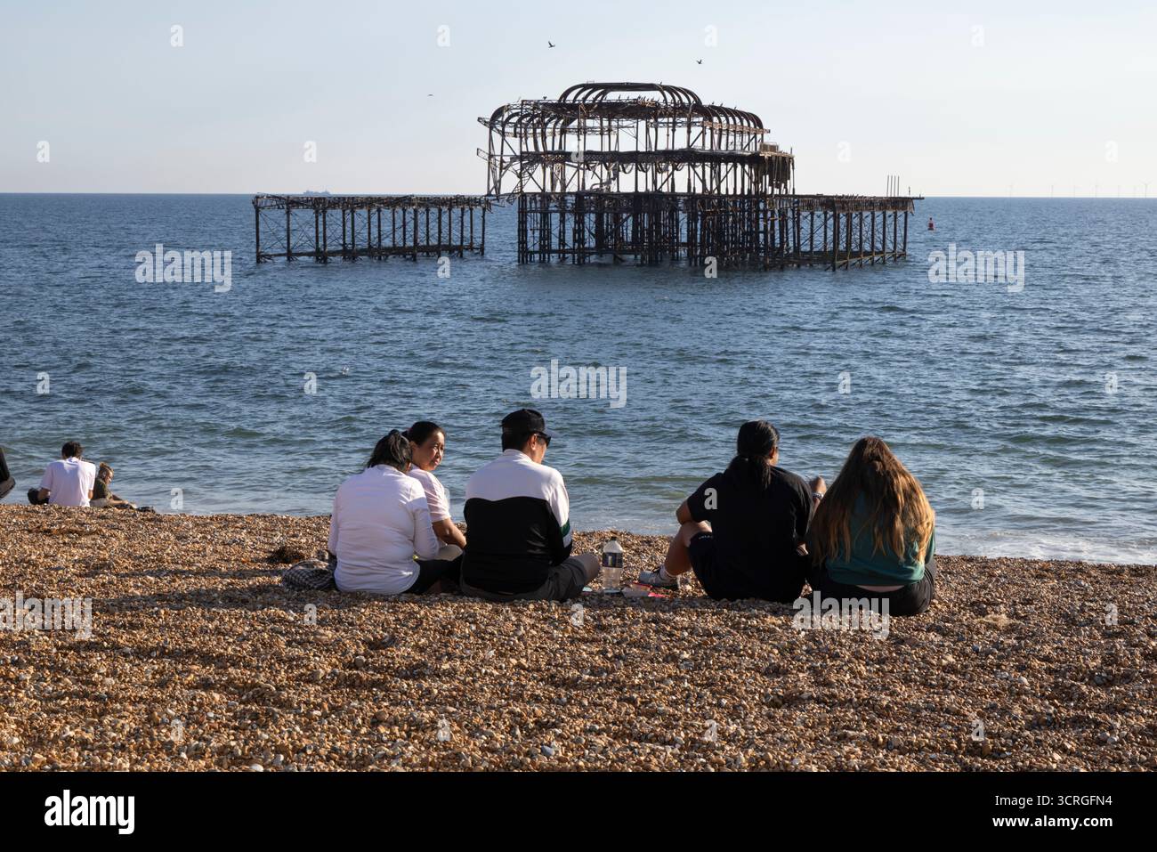 People sitting on beach in afternoon sunshine with Brighton West Pier behind, Brighton, East Sussex, England, United Kingdom, Europe Stock Photo