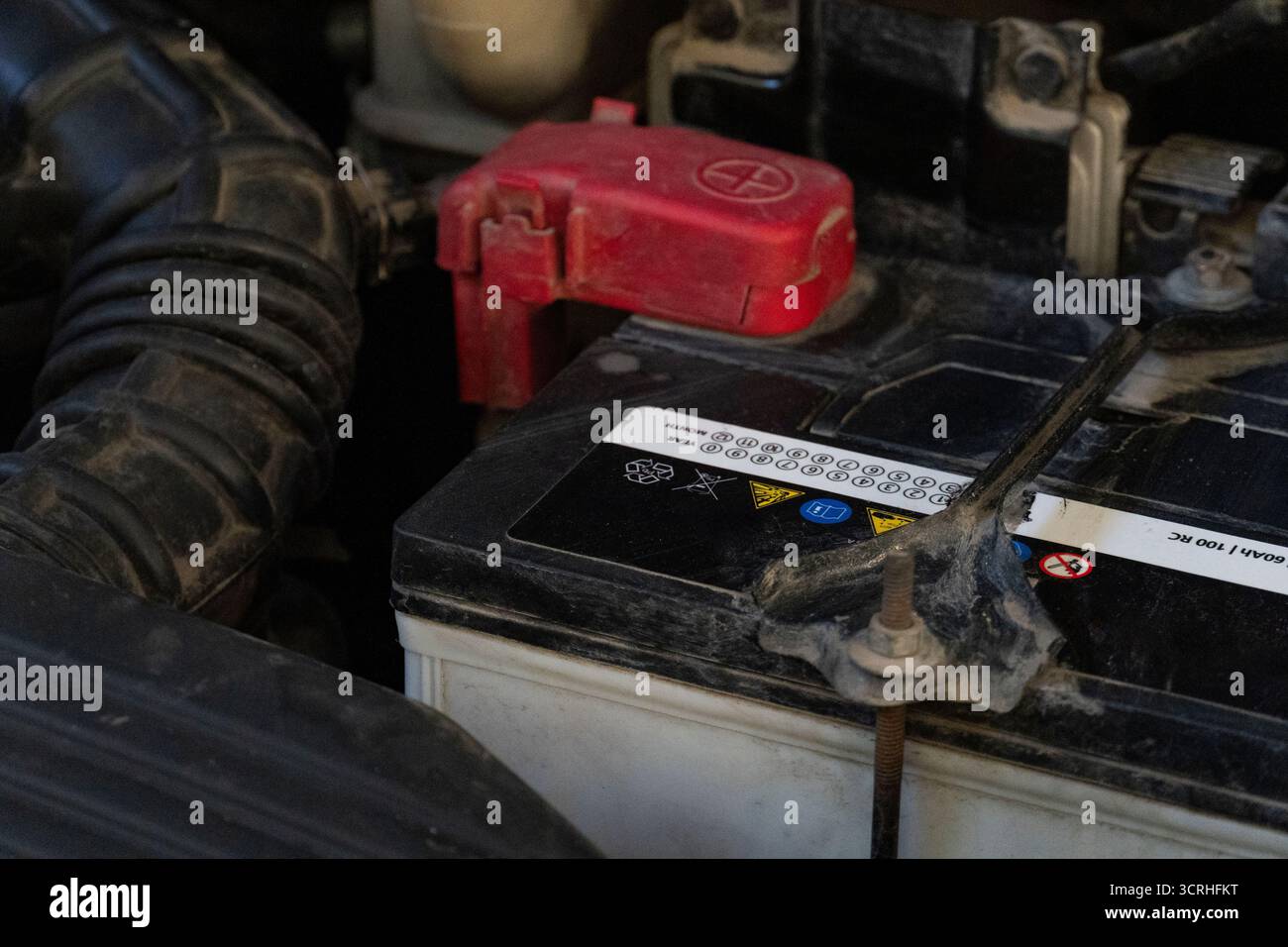 Close-up view of a dusty car battery with a red positive terminal cap ...