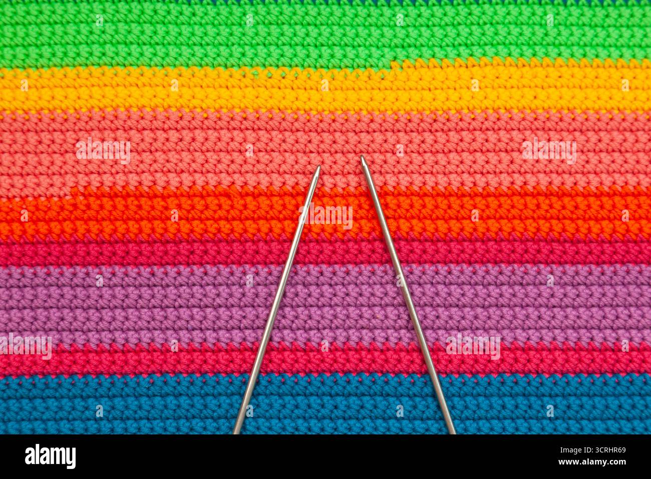 Knitted multi-colored handmade fabric with two knitting needles. Stock Photo