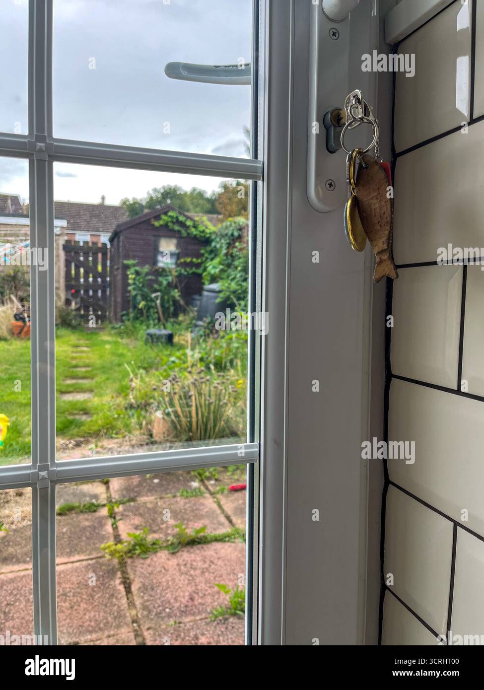 A key with keychains is inserted into the keyhole of a glass door overlooking an English garden - Smartphone Captured Stock Image