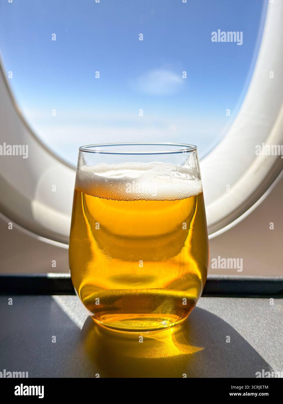 Close up view of a glass of lager beer in front of the window of a business class cabin of a passenger plane. No people. - Smartphone Captured Stock Image