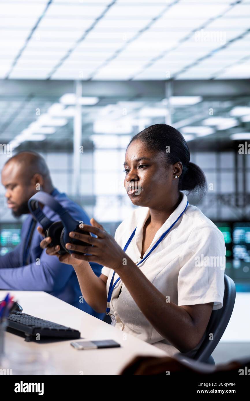 Woman in data center putting headphones on while using programming languages to construct applications. Server hub employee listening podcasts to make time pass faster while debugging code Stock Photo