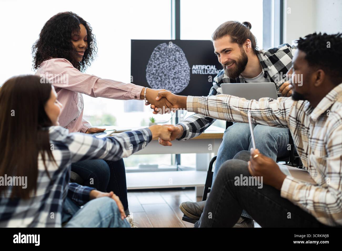 Diverse team celebrates success with a handshake in a tech environment Stock Photo