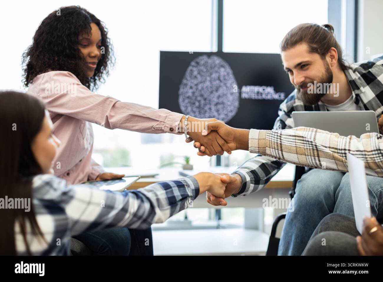 Diverse team celebrates success with a handshake in a tech environment Stock Photo