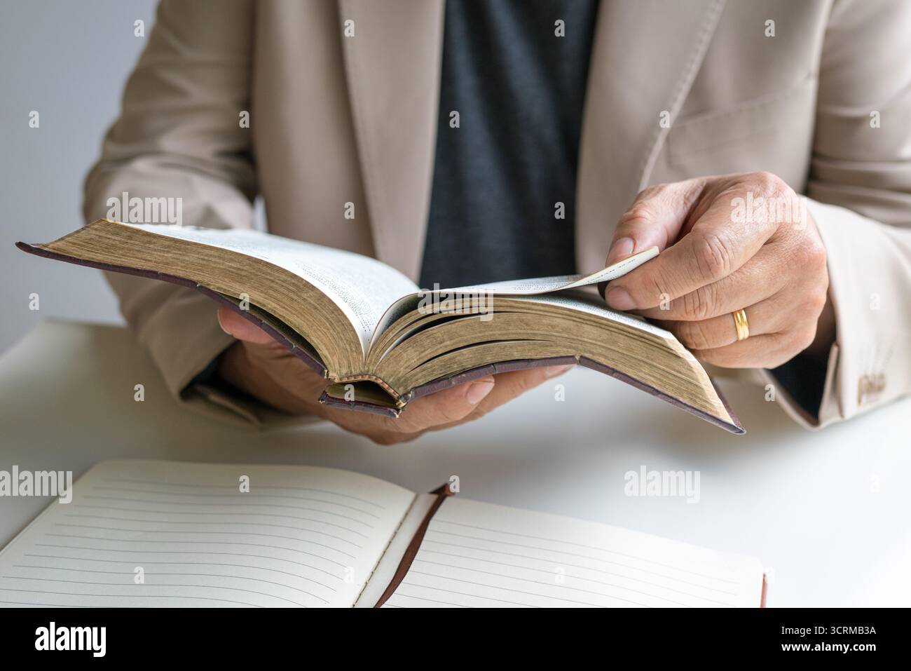 Preacher holding an open old rustic bible in his hands, with a notepad on top of desk. Stock Photo
