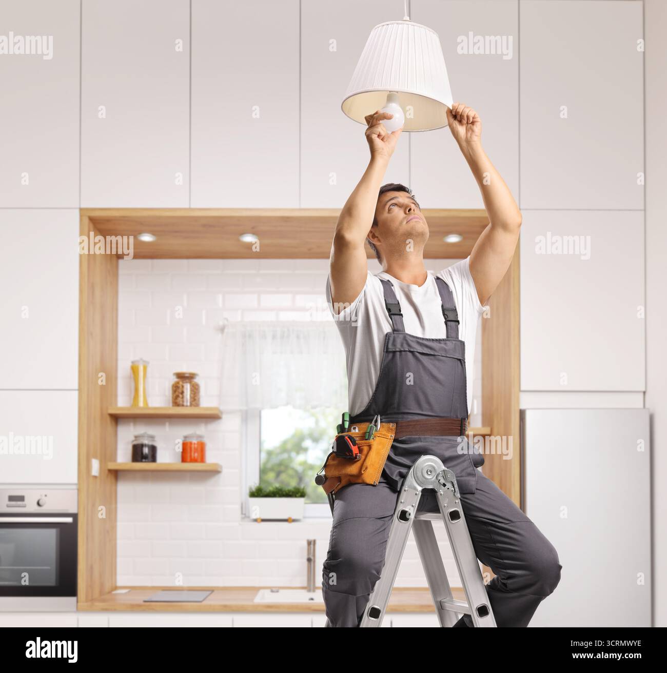 Repairman on a ladder changing a light bulb on a kitchen ceiling Stock ...