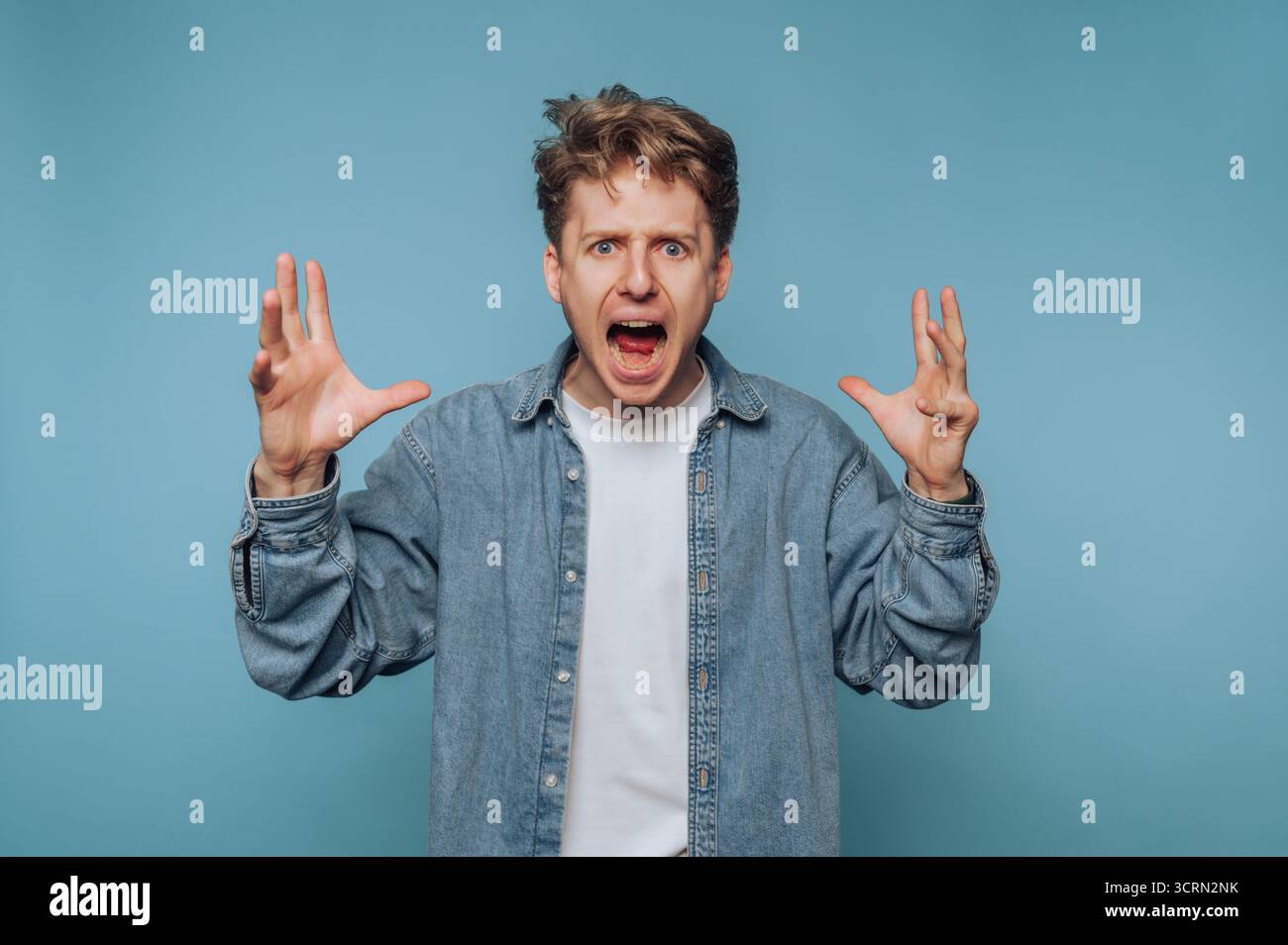 Man expressing frustration with hands raised in a blue background setting Stock Photo