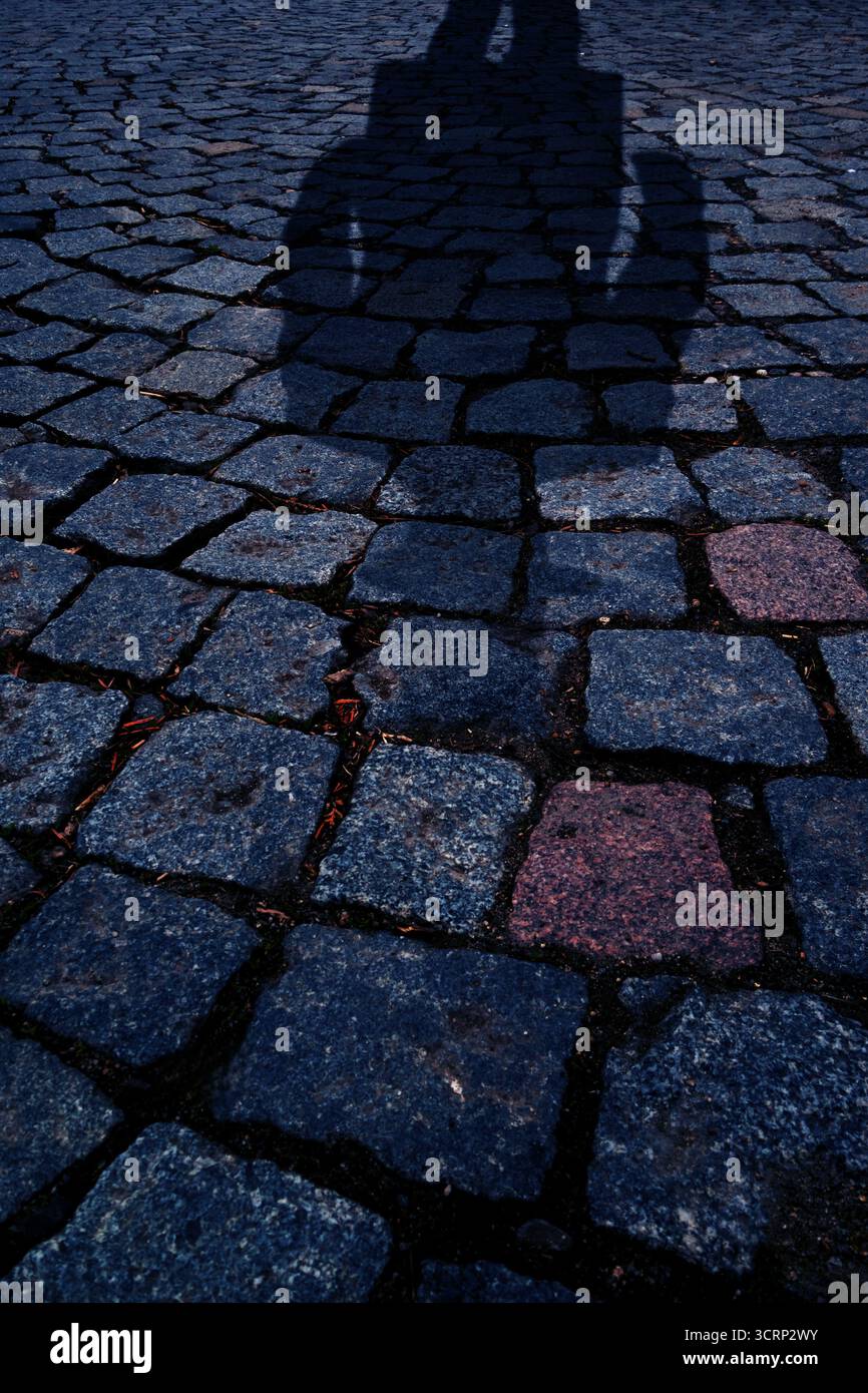 Shadow of a man cast on cobblestone street, abstract urban background with stone pavement Stock Photo