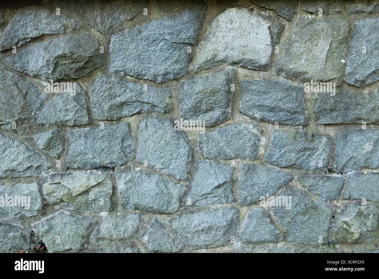 Stone wall with irregular grey rocks, rustic background texture of masonry construction Stock Photo