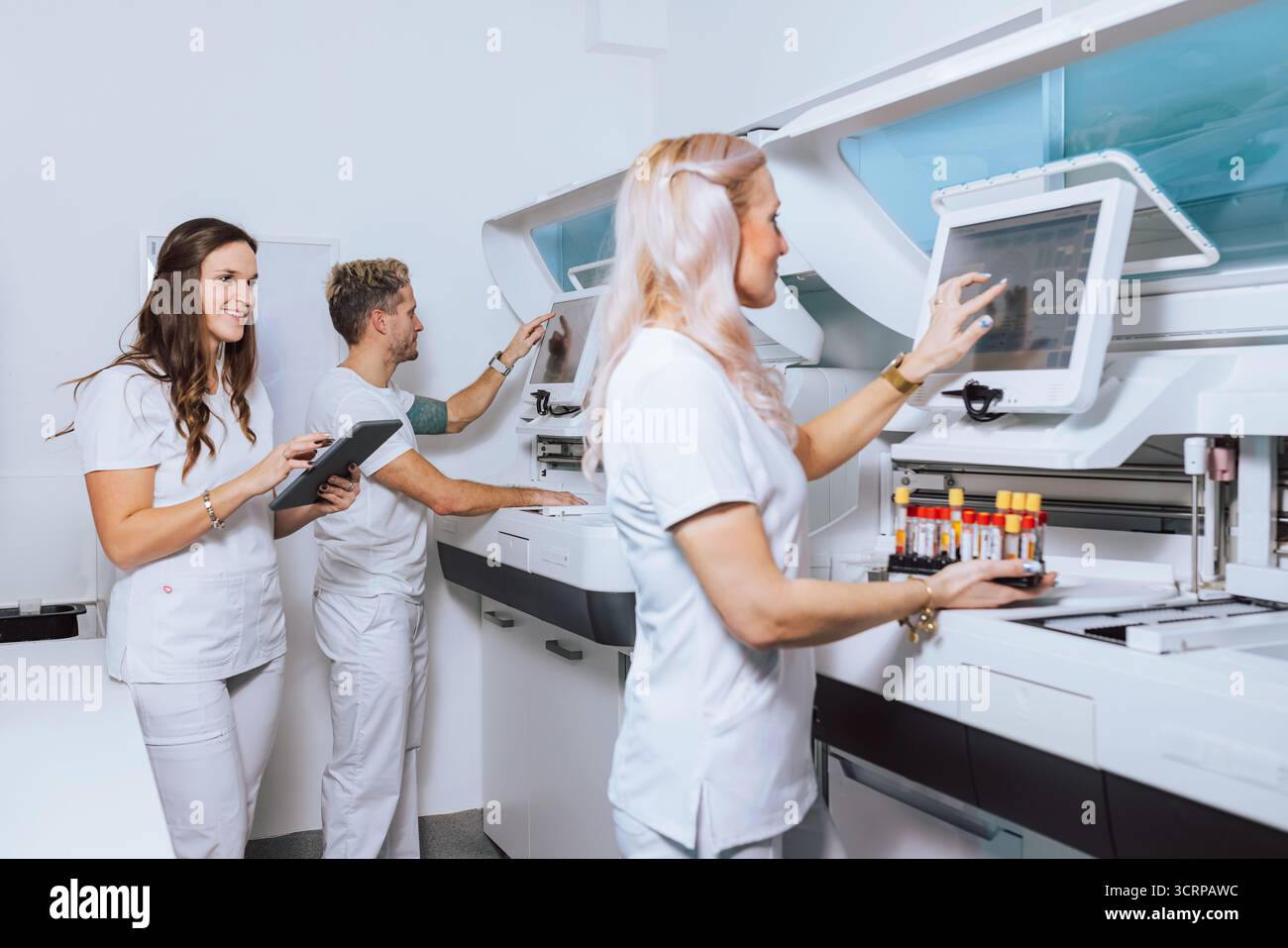 Medical professionals in a lab process samples using advanced equipment while collaborating on tasks and managing data. Stock Photo