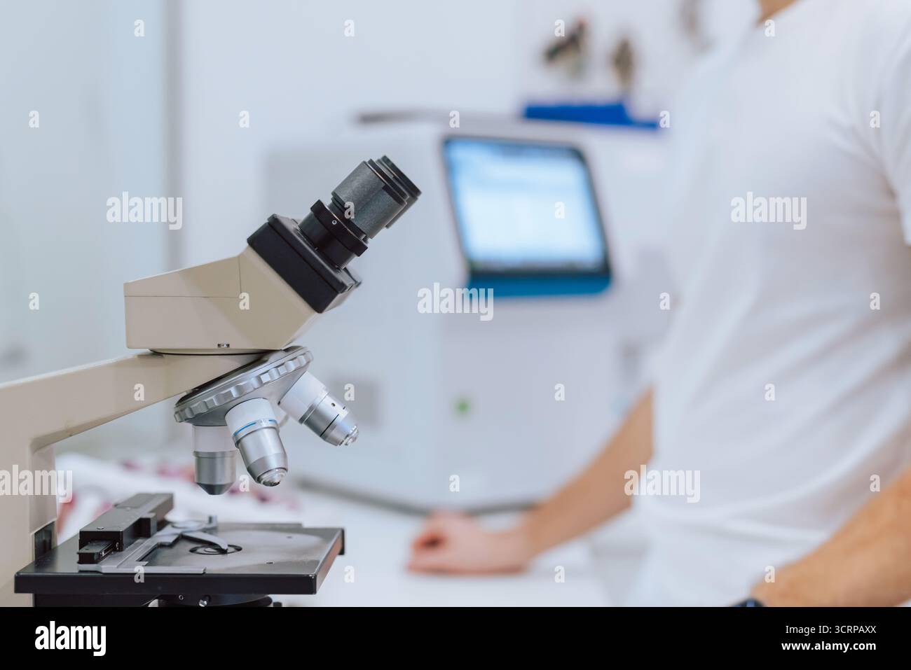 A scientist in a white shirt analyzes samples through a microscope in a modern laboratory setting. Stock Photo