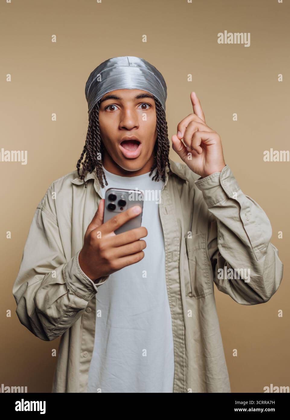 Young man with surprised expression holding smartphone, pointing up. Stock Photo