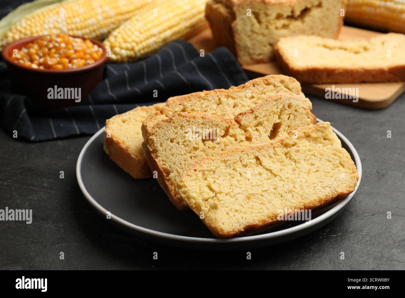Freshly baked cornbread, cobs and seeds on black table, closeup Stock Photo