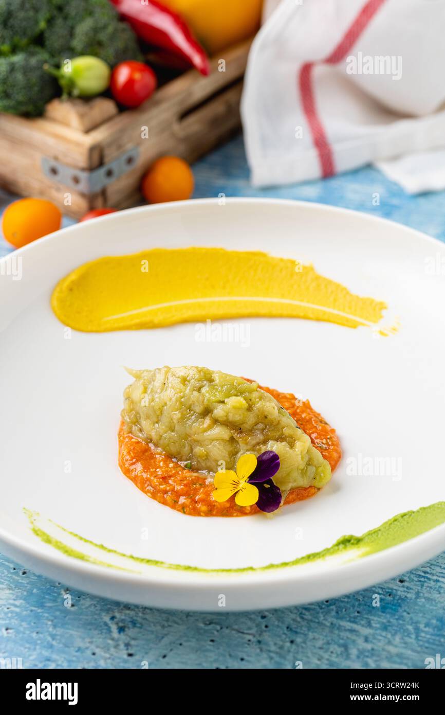 Eggplant puree with colorful sauces and edible flower garnish Stock Photo