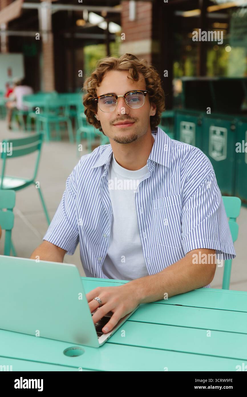 Man working on laptop at cafe, looking confidently ahead. Stock Photo