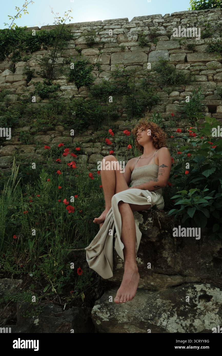 Woman lost in thought sitting by nature wall Stock Photo