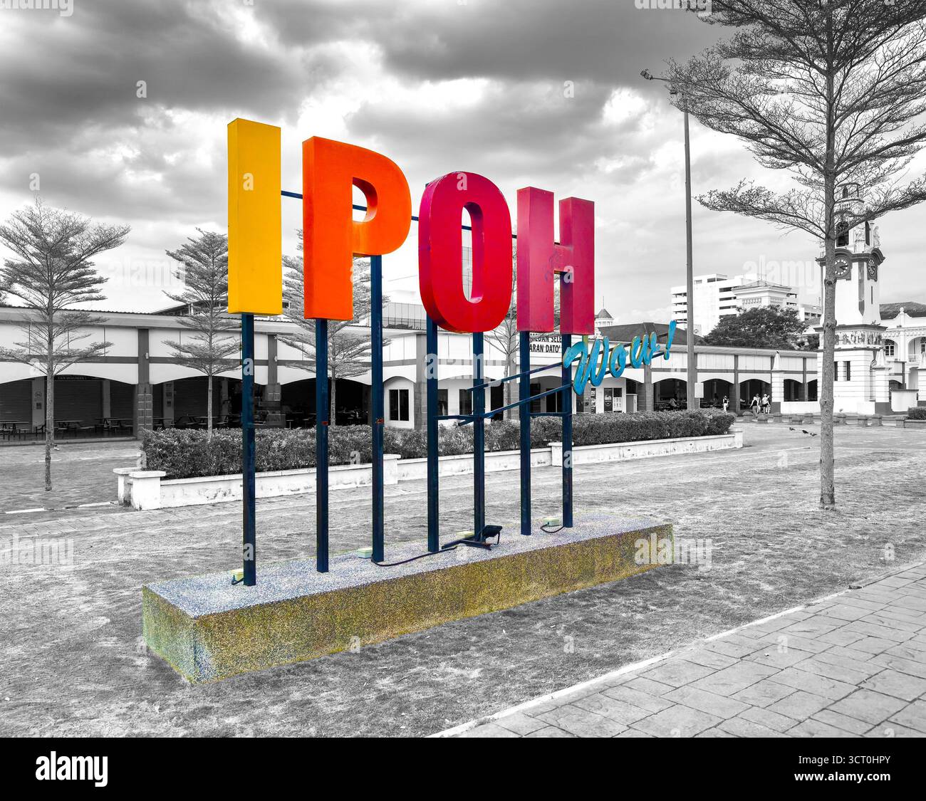 Colorful 'Ipoh' sign sculpture in an urban park with a backdrop of black and white architecture under a dramatic cloudy sky - Smartphone Captured Stock Image