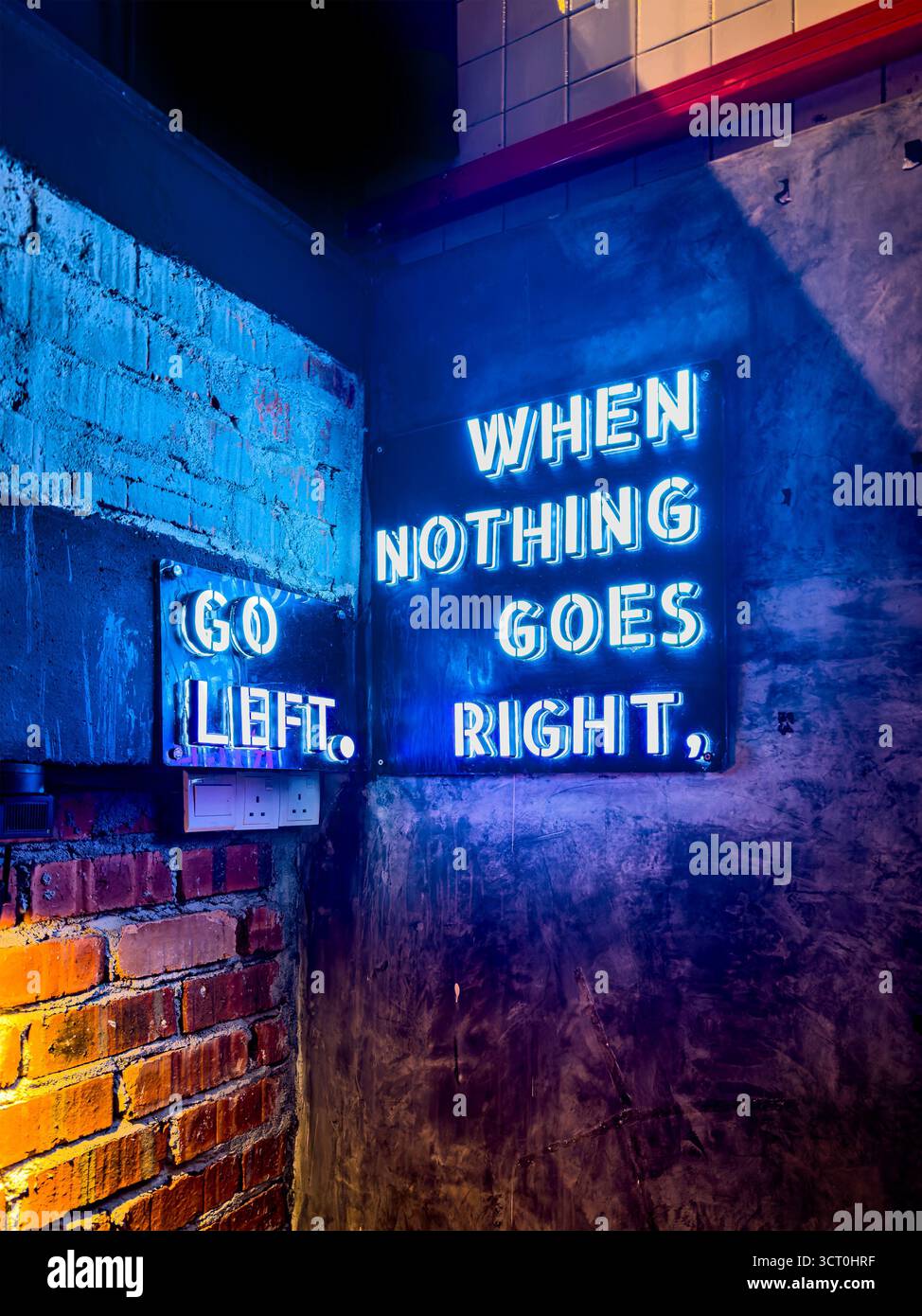 Neon signs on a brick wall with phrases 'Go Left' and 'When Nothing Goes Right' glowing incafe restaurant Ipoh malaysia - Smartphone Captured Stock Image
