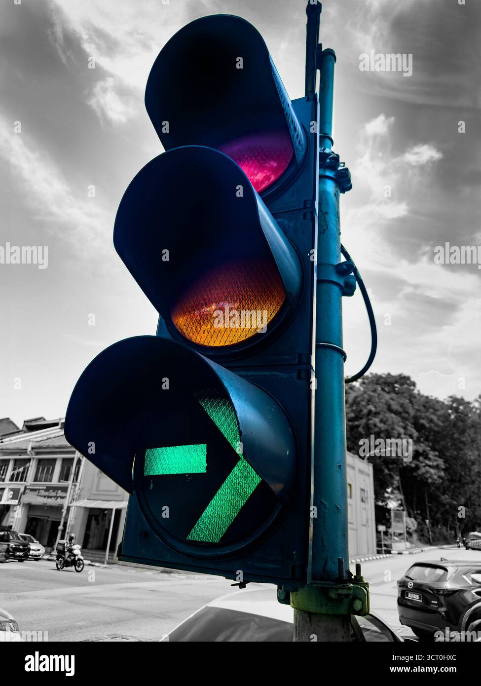 Traffic light with a green filter arrow at an intersection in a city, with cars and buildings in the background under a cloudy sky - Smartphone Captured Stock Image