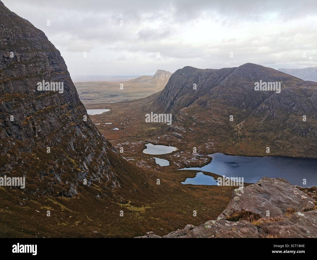 View from Sgùrr an Fhìdhleir on North Coast 500—Lochan Tuath and Beinn an Eoin framed by dramatic Highland peaks and wilderness with moody grey sky. - Smartphone Captured Stock Image