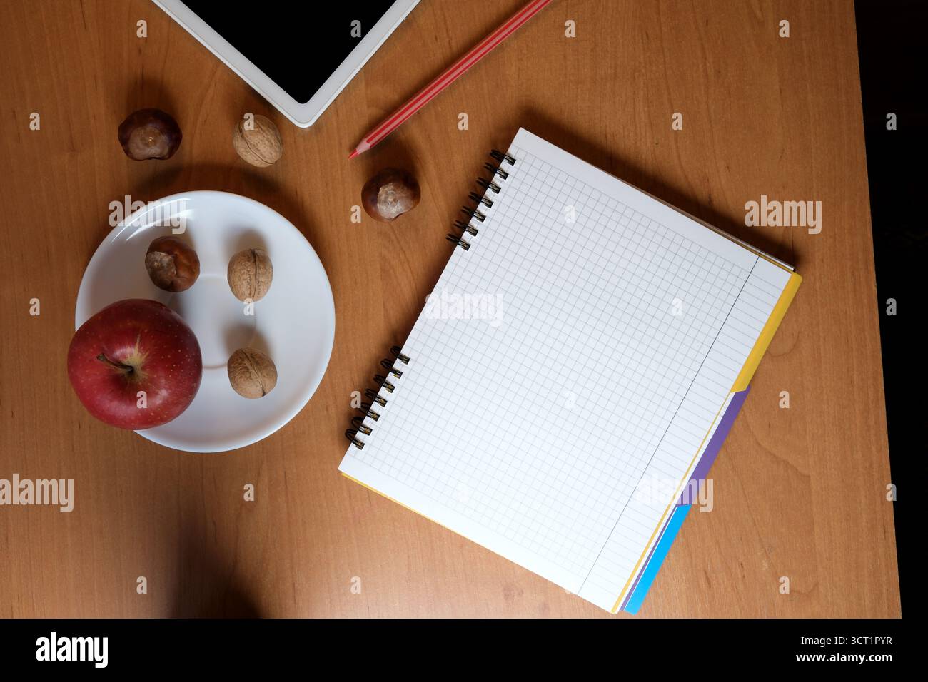 A warm workspace features a notepad, fresh apple, and nuts, inviting creativity. Stock Photo