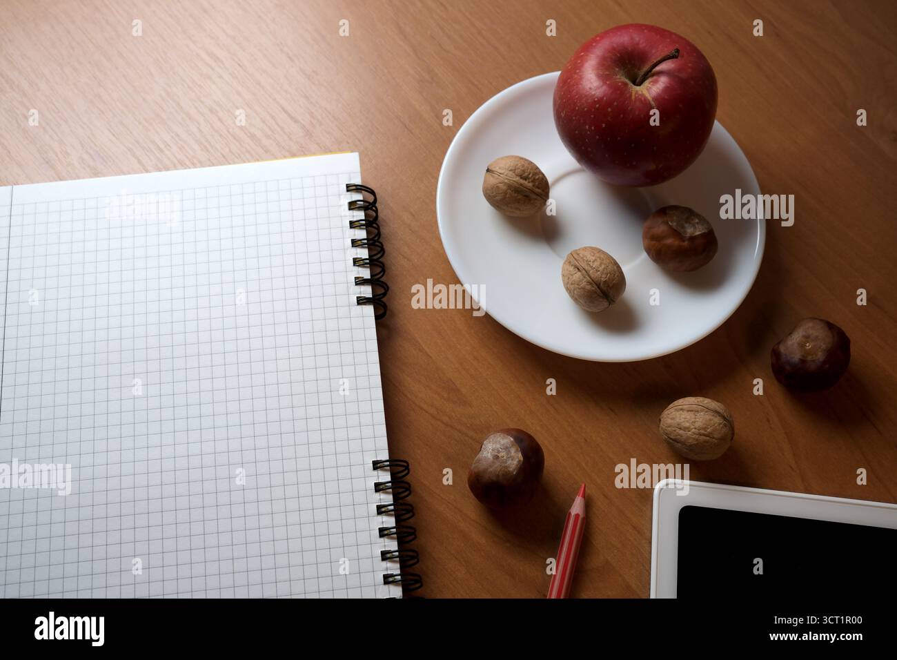 A cozy workspace featuring a notebook, an apple, and nuts on a wooden table. Stock Photo