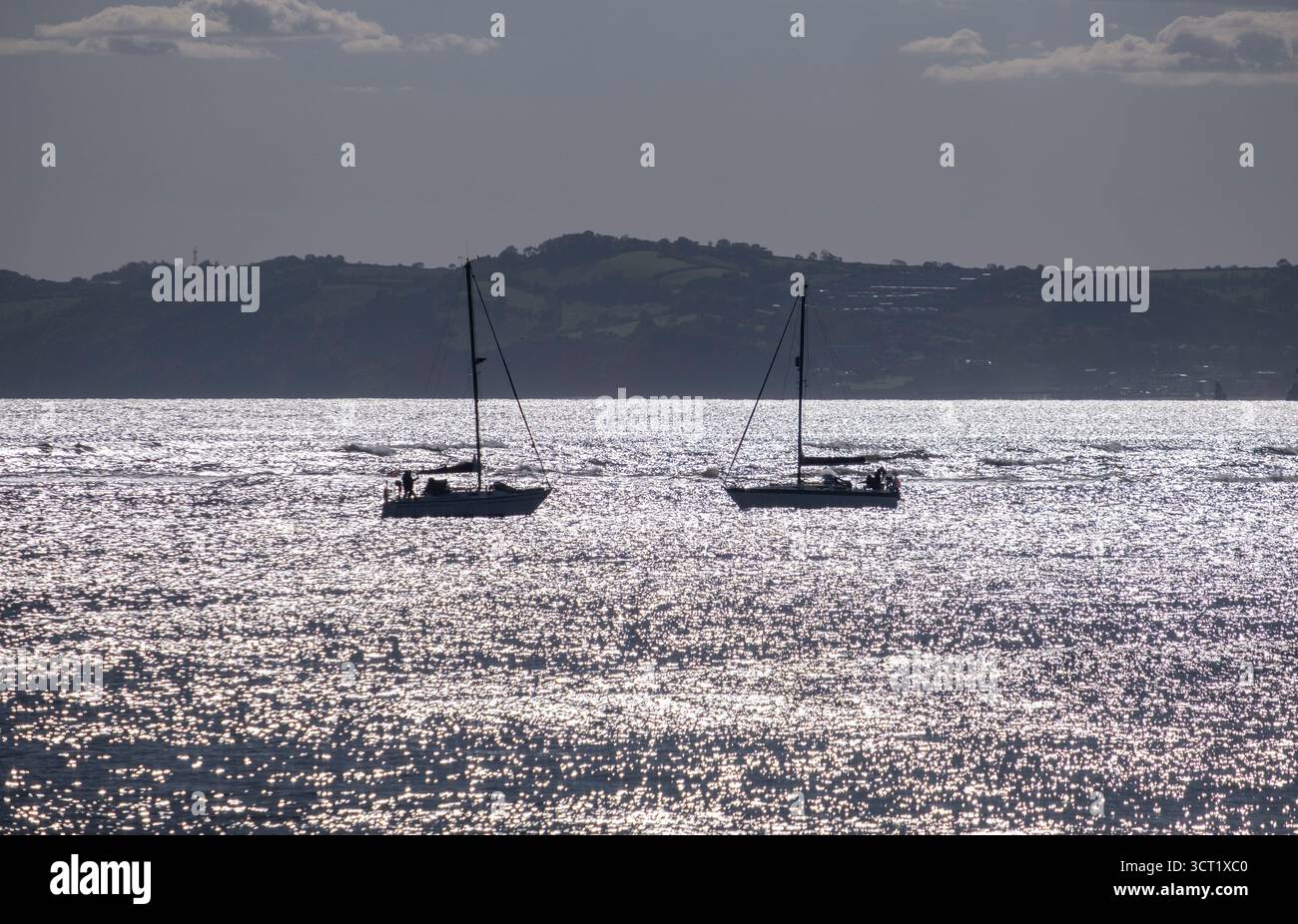 Two sailing yachts psss each other at dusk in Sidmouth, Devon, England. Stock Photo