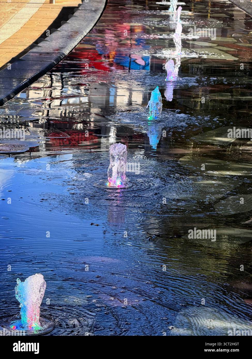 Fountain lit by colourful lights in Exchange Square in Manchester City centre - Smartphone Captured Stock Image