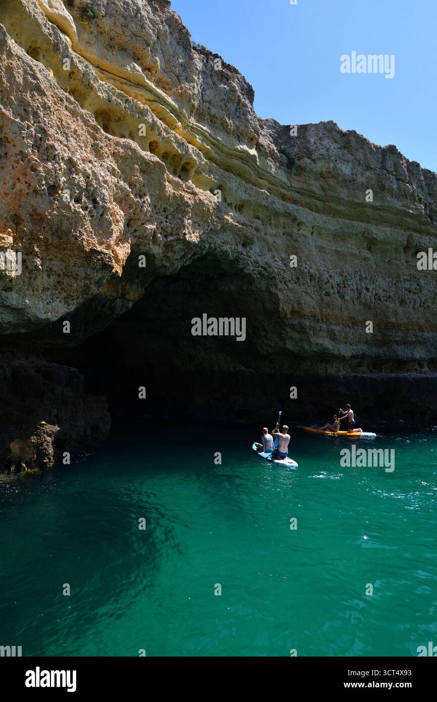 Paddle boarders explore one of the many caves along the Algarve coastline in Portugal. Stock Photo