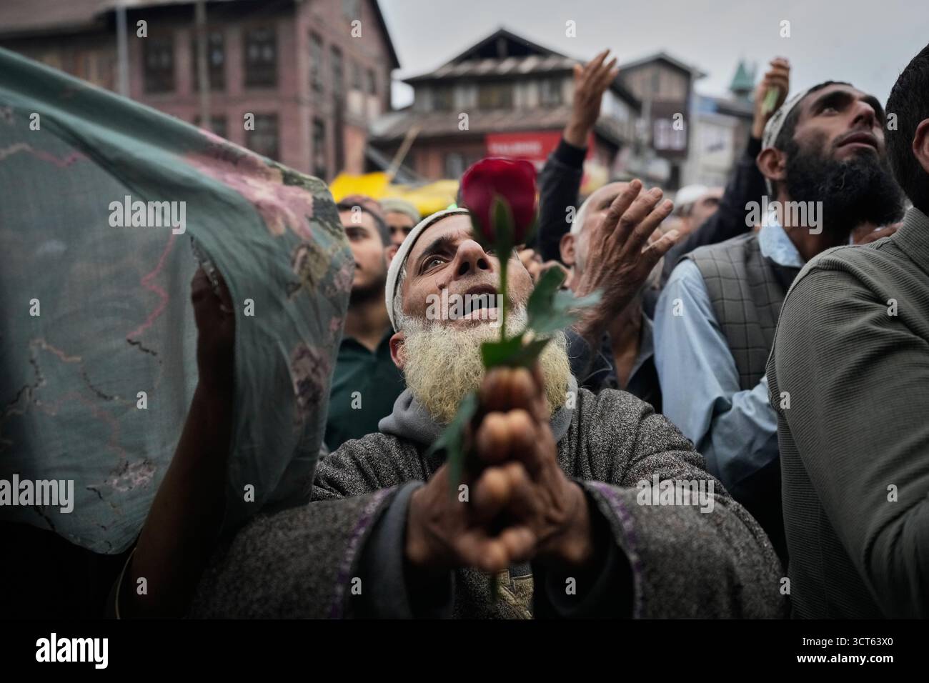 An elderly Kashmiri Muslim man holds a rose and pray as priest displays ...