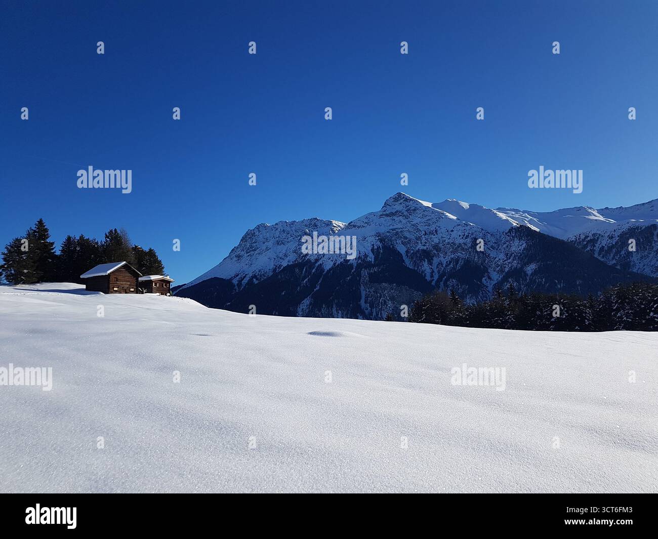 Idyllic and beautiful winter landscape in the Swiss Alps with typical wooden mountain huts on a bright and sunny winter day, Switzerland Stock Photo
