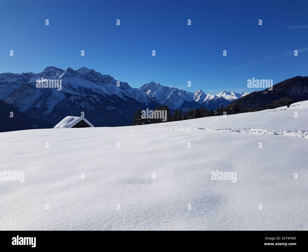 Idyllic and beautiful winter landscape in the Swiss Alps with typical wooden mountain huts on a bright and sunny winter day, Switzerland Stock Photo