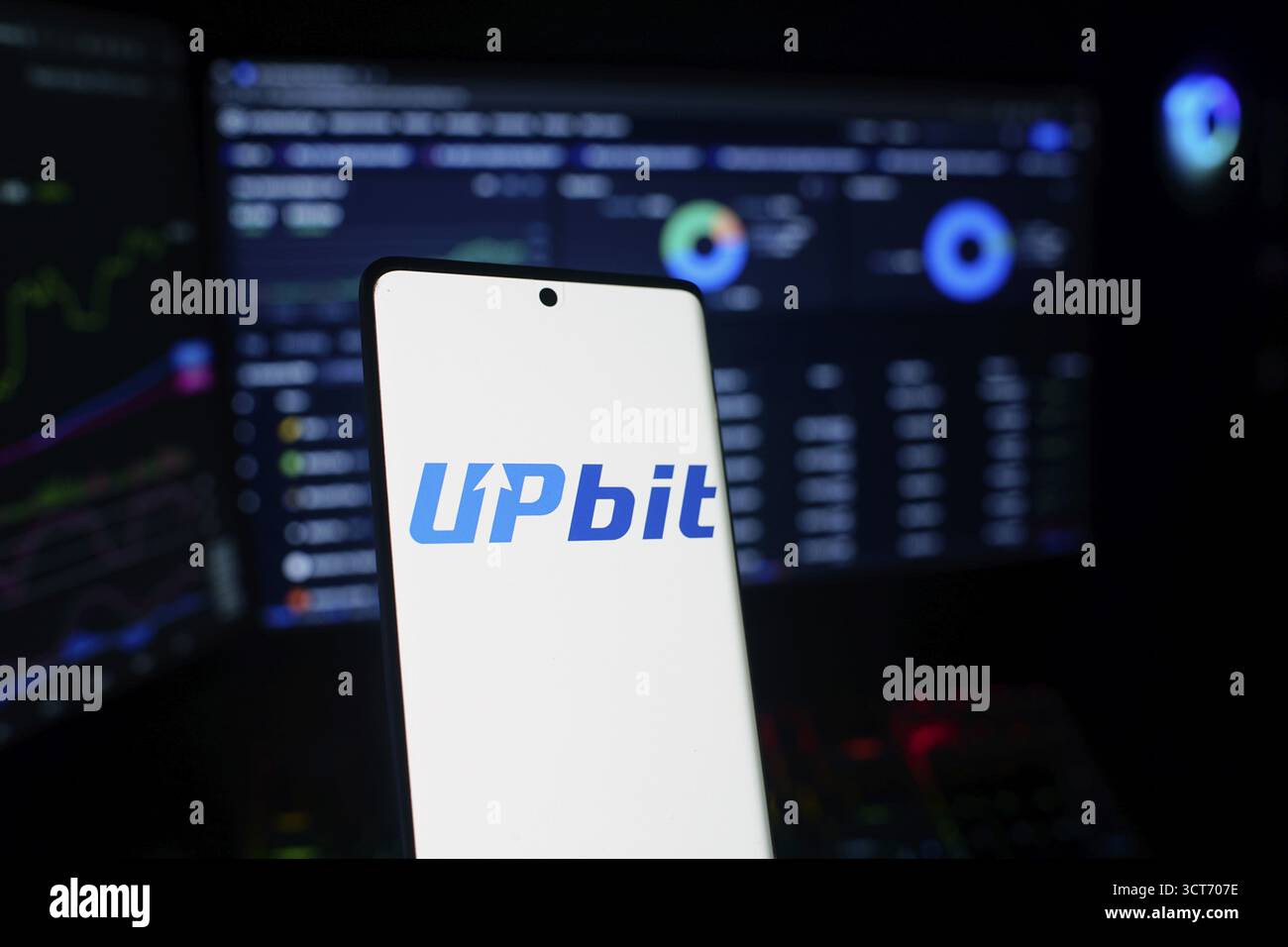 Smartphone displaying Upbit logo in front of financial data screens ...