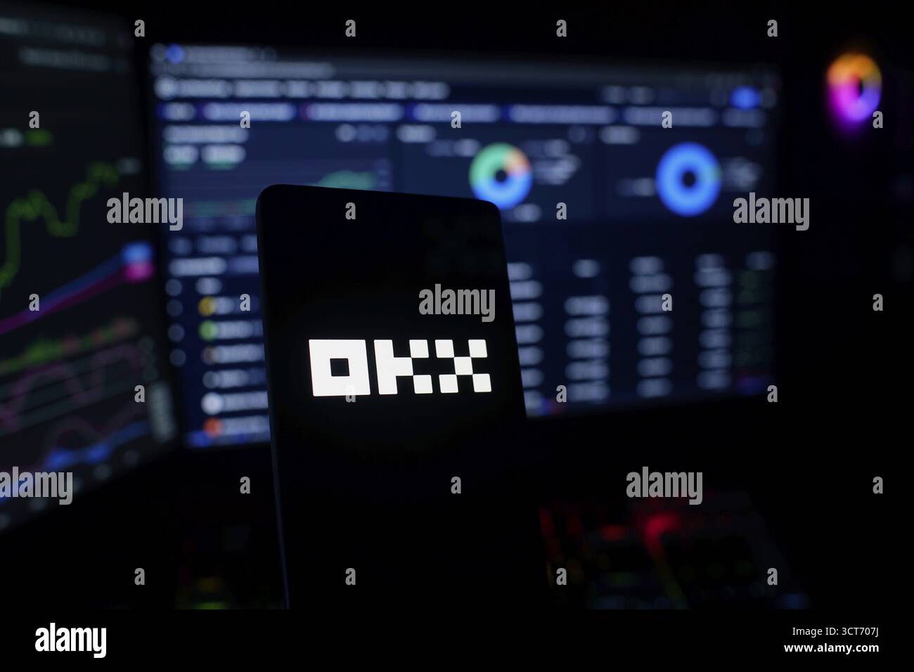 Dark-themed image showing OKX logo with financial charts in the background Stock Photo