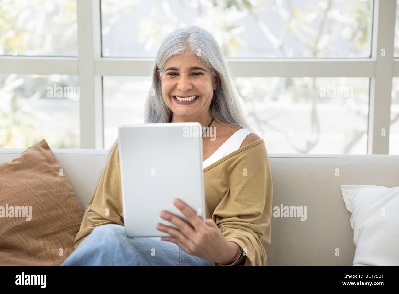 Happy senior grey haired woman using tablet pc Stock Photo