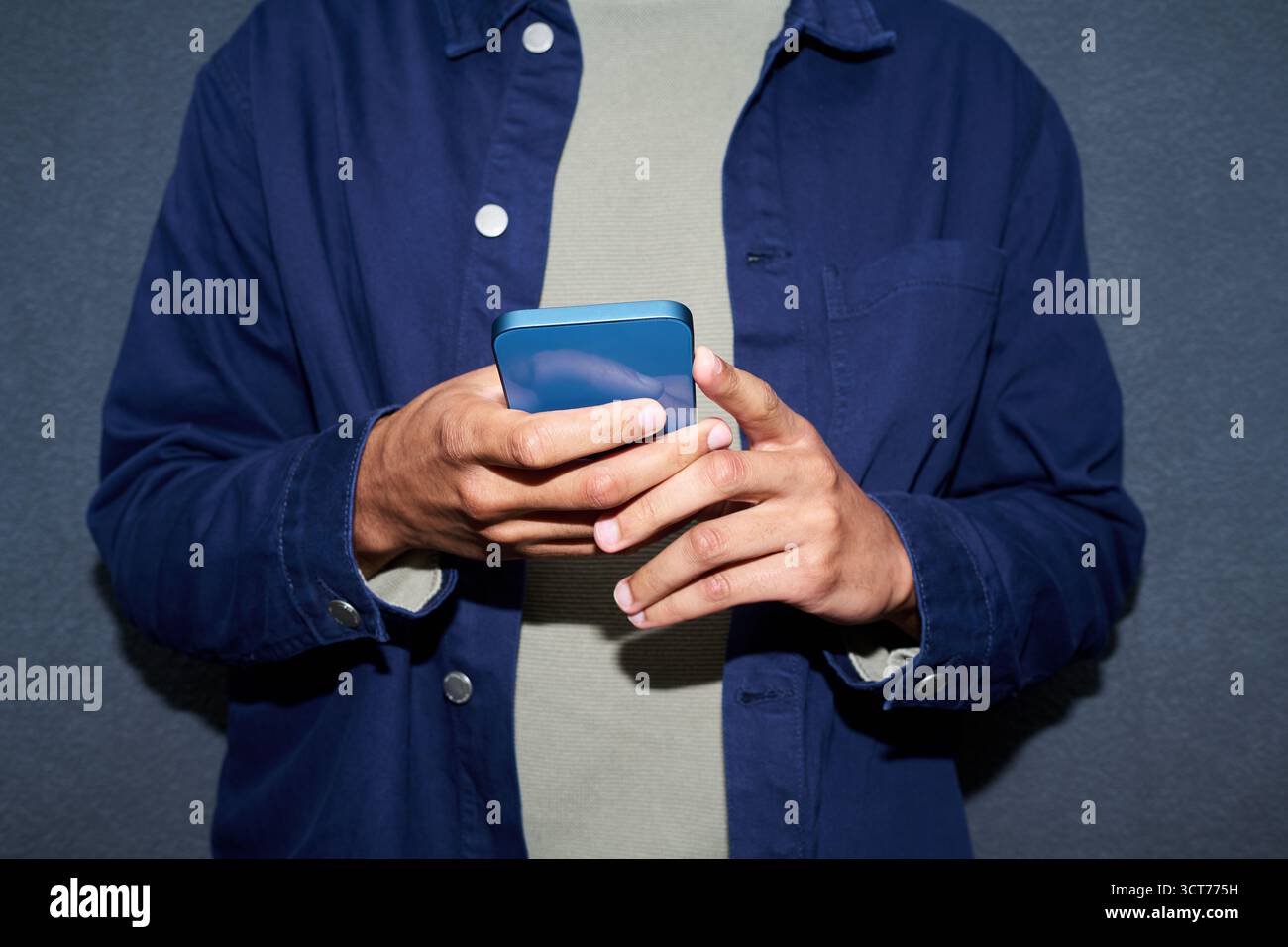 Young Man Using Smartphone While Standing Against Wall Stock Photo