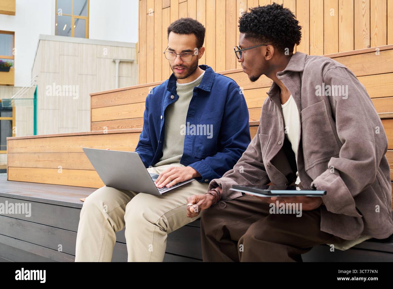 Young Multiethnic Men Collaborating Outdoors Using Laptop and Tablet Stock Photo