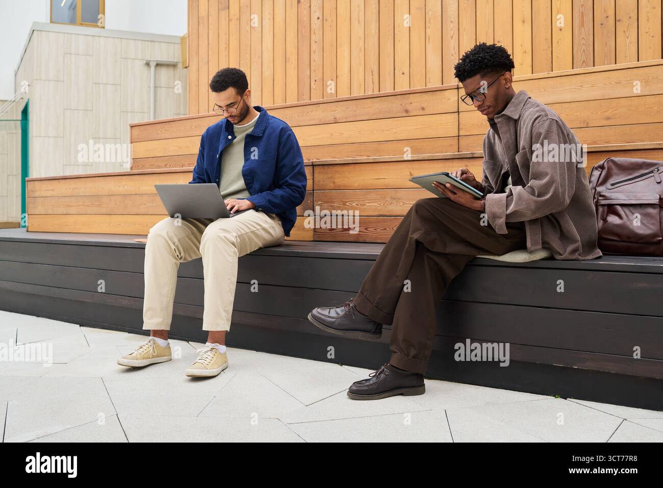 Young Man and Black Man Working Remotely Using Laptop and Tablet Stock Photo