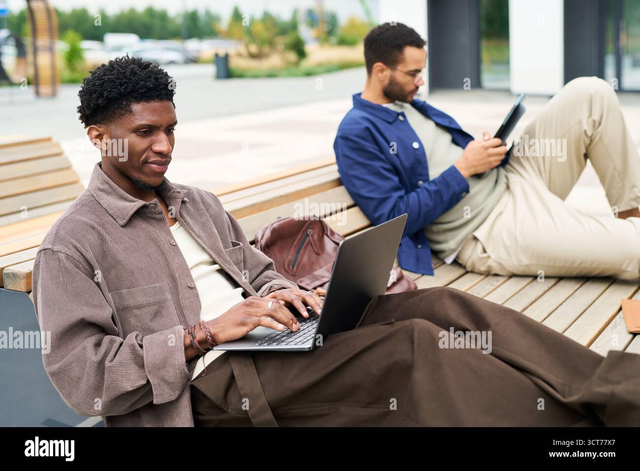 Two Young Men Using Devices Outdoors Stock Photo