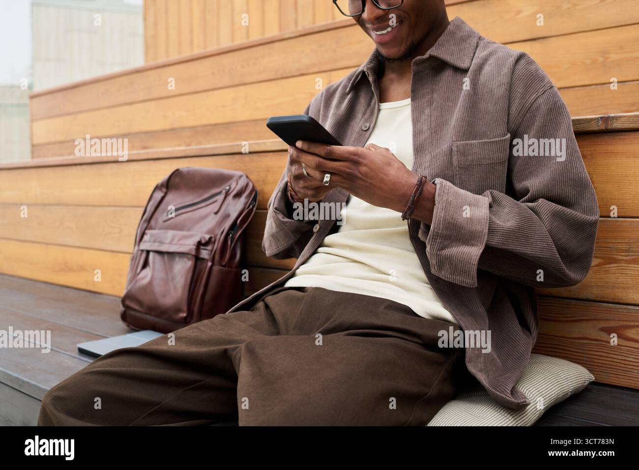 Young Black Man Sitting Outdoors Using Smartphone and Smiling Stock Photo