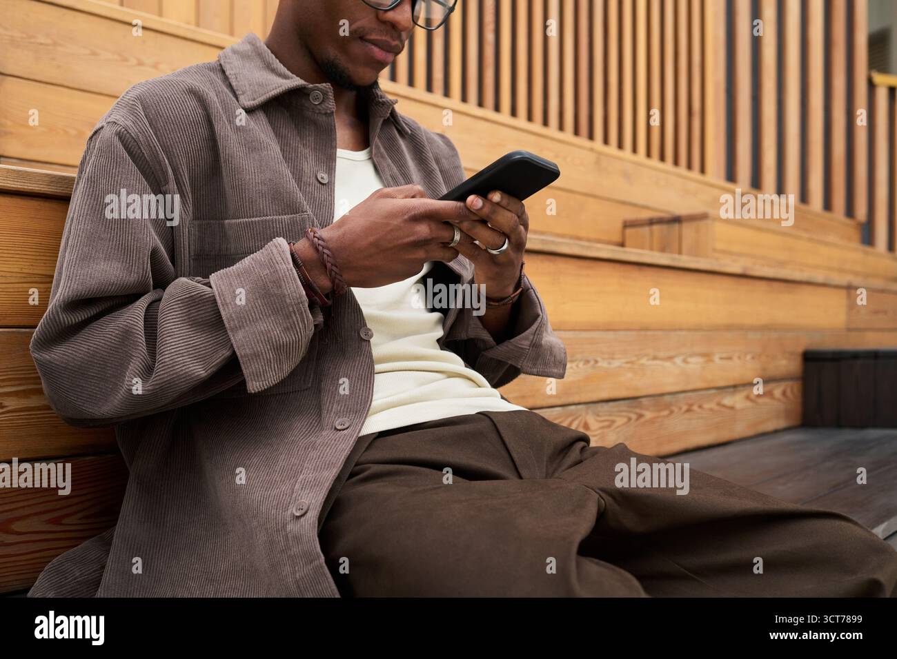 Young Black Man Sitting Outdoors Using Smartphone for Messaging Stock Photo