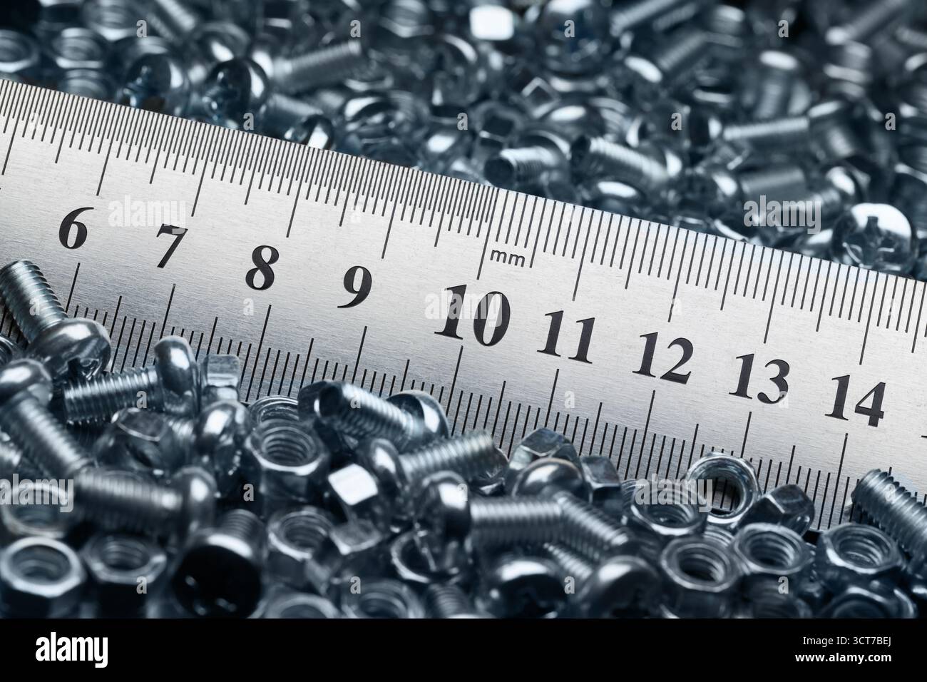 Lots of small screws and nuts scattered in a heap and a metal ruler Stock Photo
