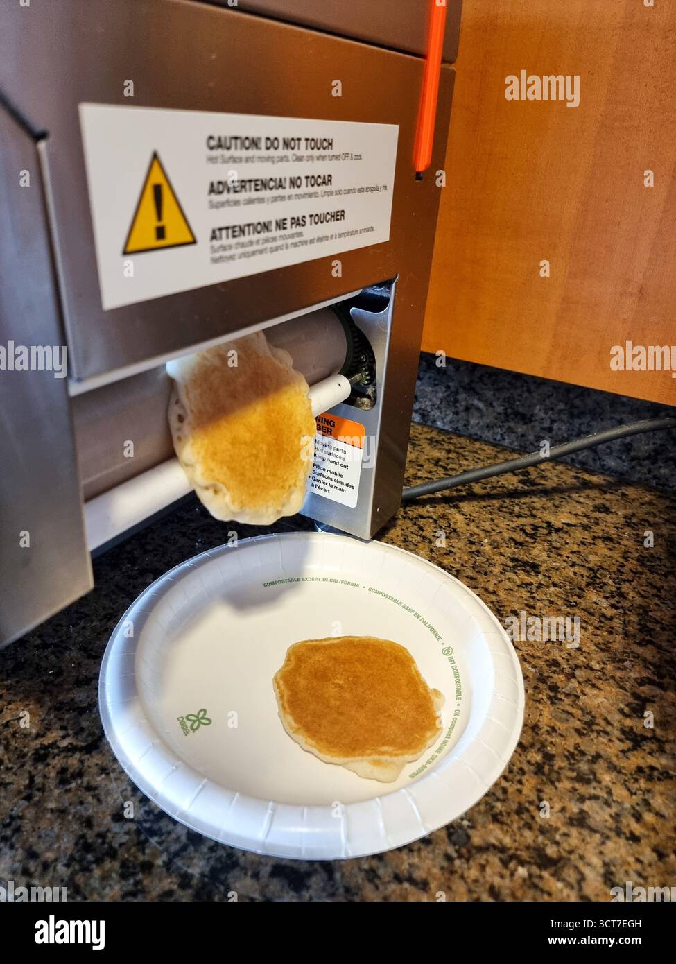 Pancake coming out of a QuickCakes: machine to make 'Fresh pancakes in a minute flat'; in a hotel breakfast room. 'Caution do not touch' - Smartphone Captured Stock Image