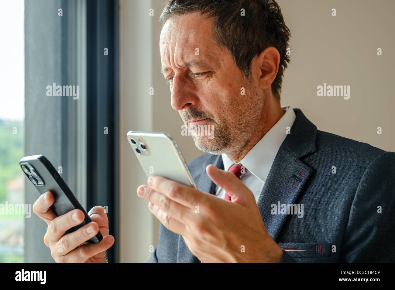 Businessman using two smartphones simultaneously, trying to synchronize data between devices. Selective focus. Stock Photo