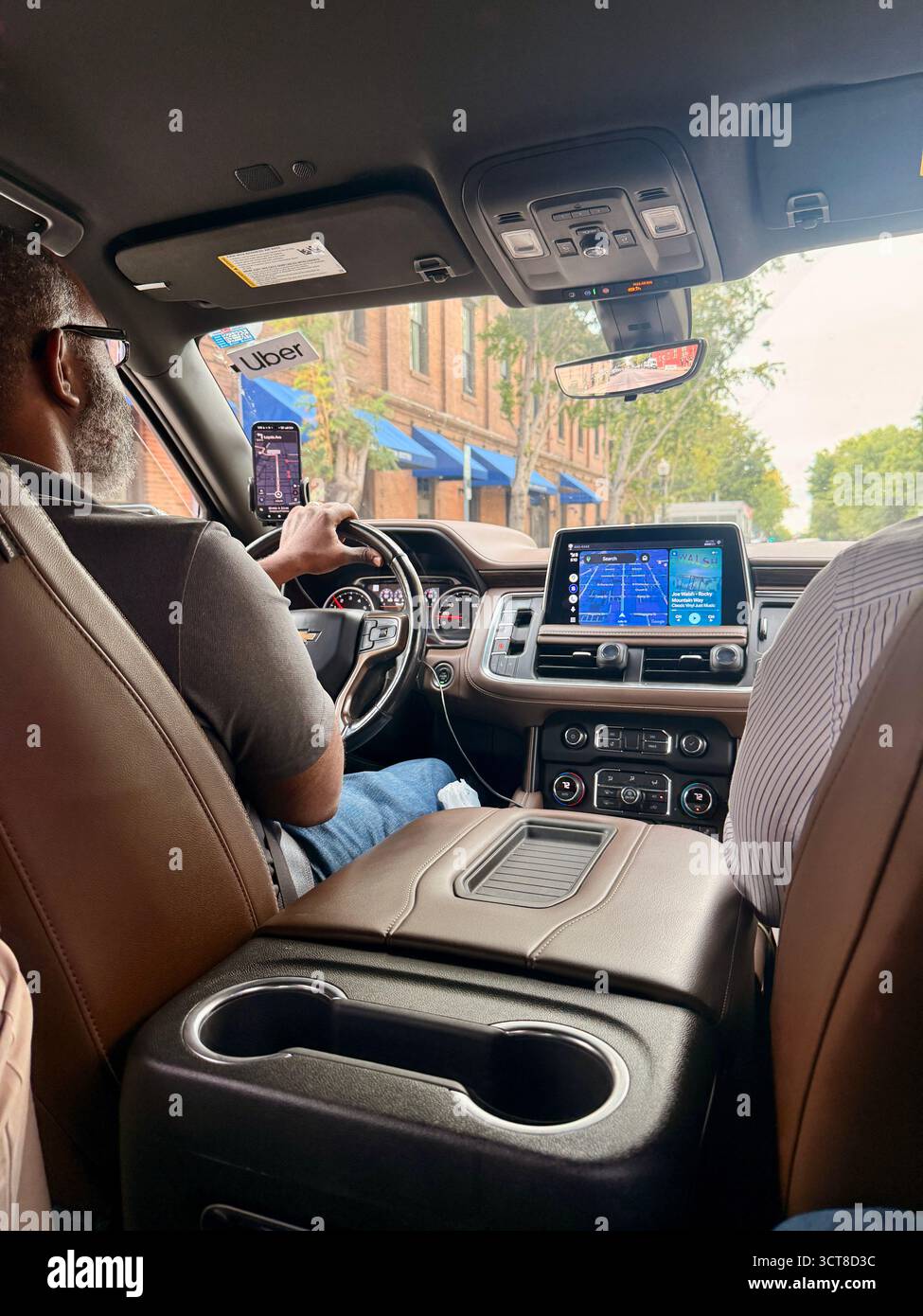 Back seat view of a modern car interior with digital dashboard and navigation screen as the driver navigates a city street lined with buildings and tr - Smartphone Captured Stock Image
